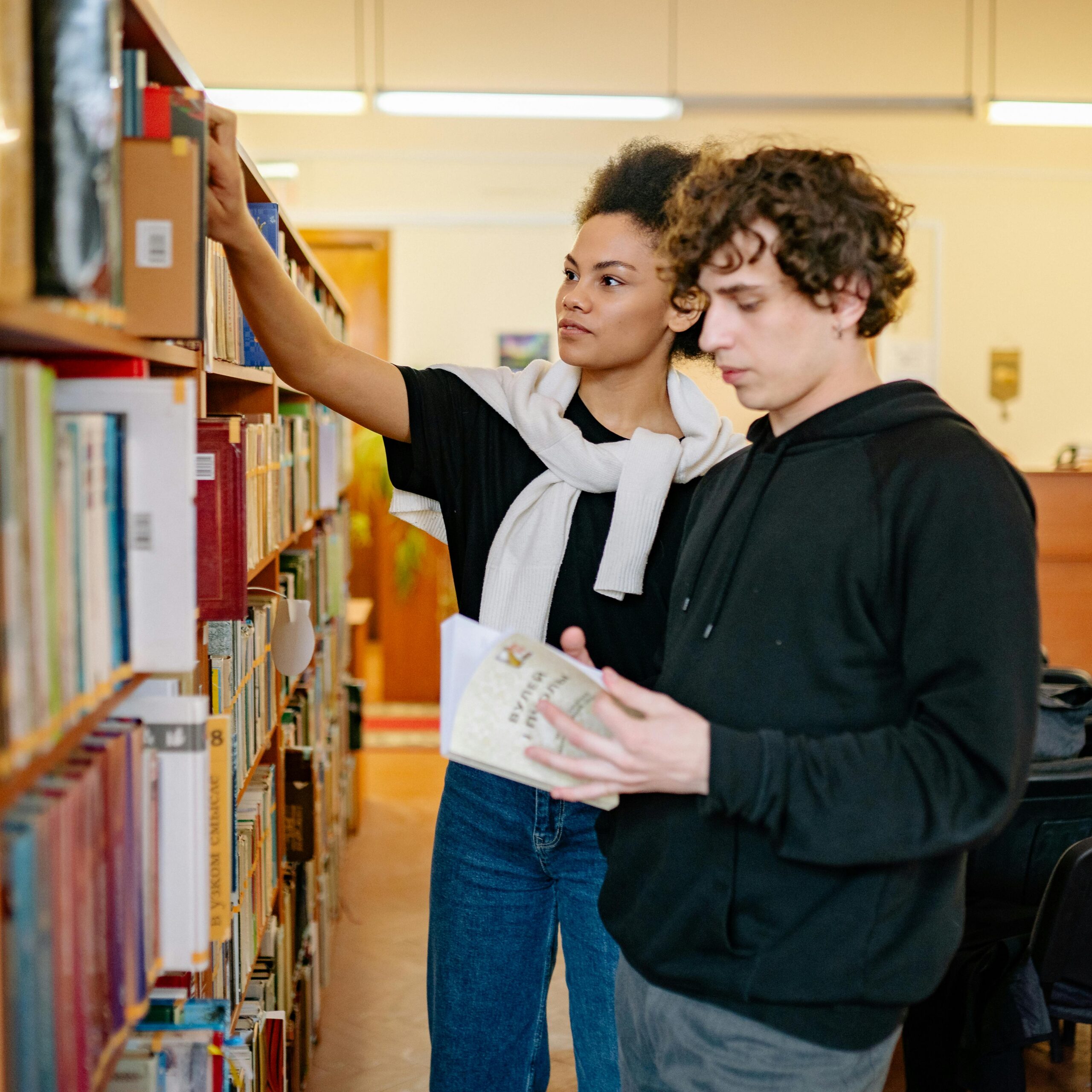 Two young adults reading and researching books in a library environment.